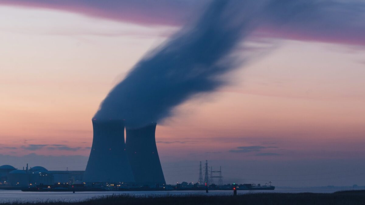skyline photography of nuclear plant cooling tower blowing smokes under white and orange sky at daytime