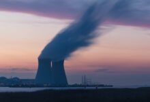 skyline photography of nuclear plant cooling tower blowing smokes under white and orange sky at daytime