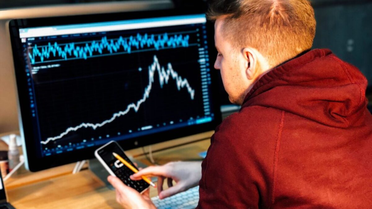 man holding black smartphone with flat screen monitor in front