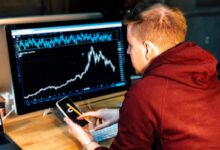man holding black smartphone with flat screen monitor in front