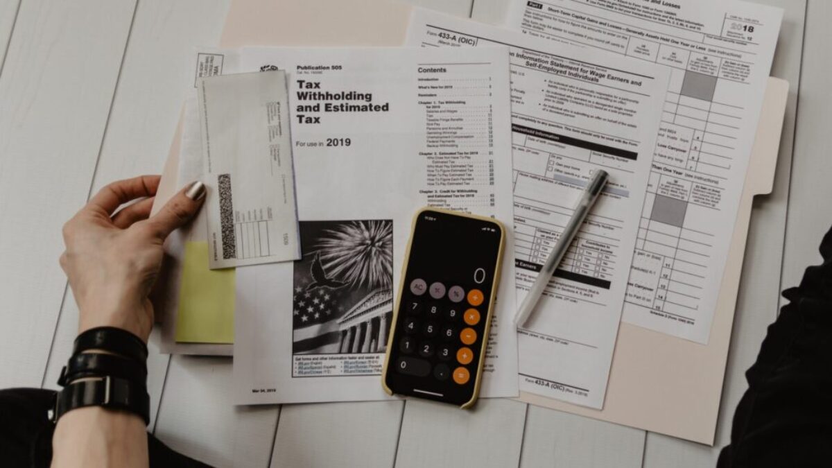 person holding paper near pen and calculator