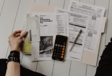 person holding paper near pen and calculator
