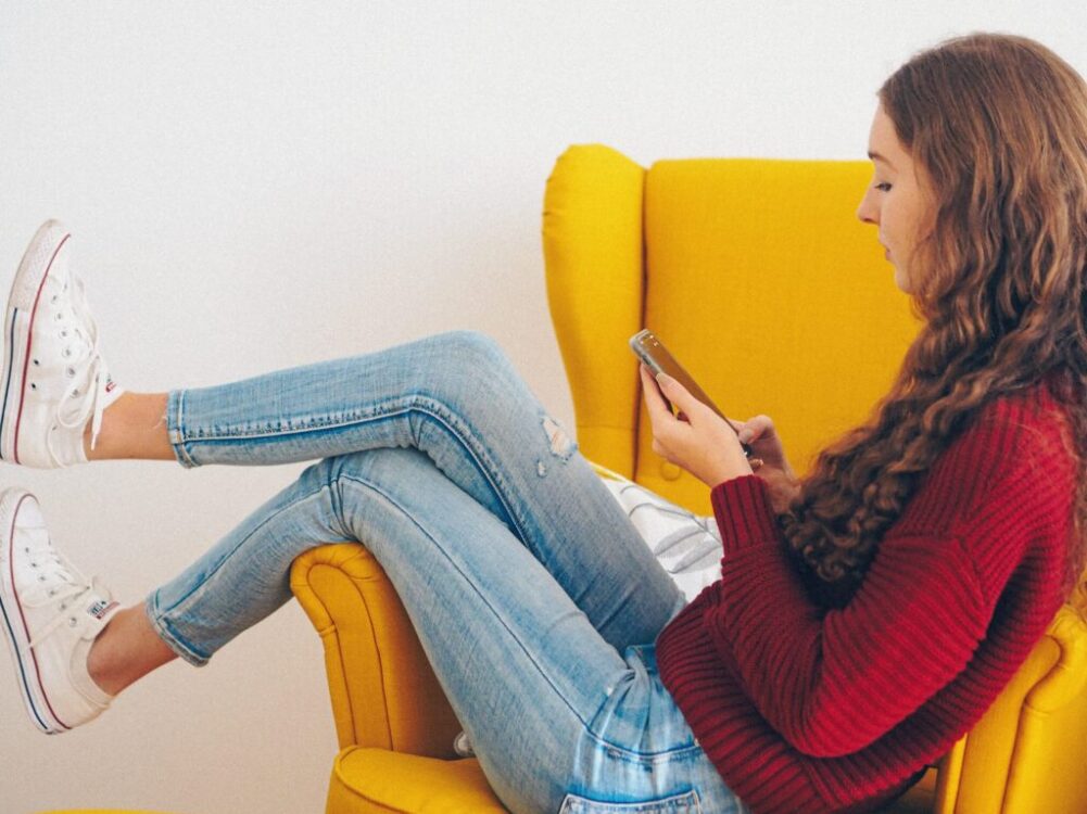 woman in red sweater and blue denim jeans sitting on yellow couch