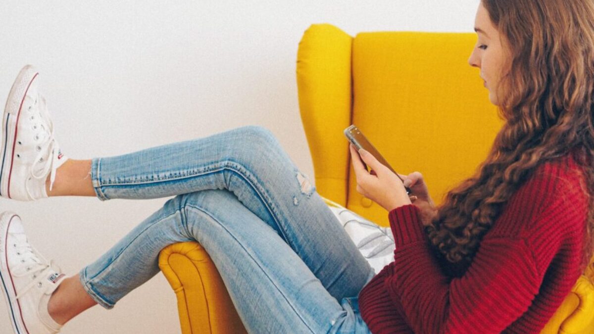 woman in red sweater and blue denim jeans sitting on yellow couch