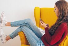 woman in red sweater and blue denim jeans sitting on yellow couch