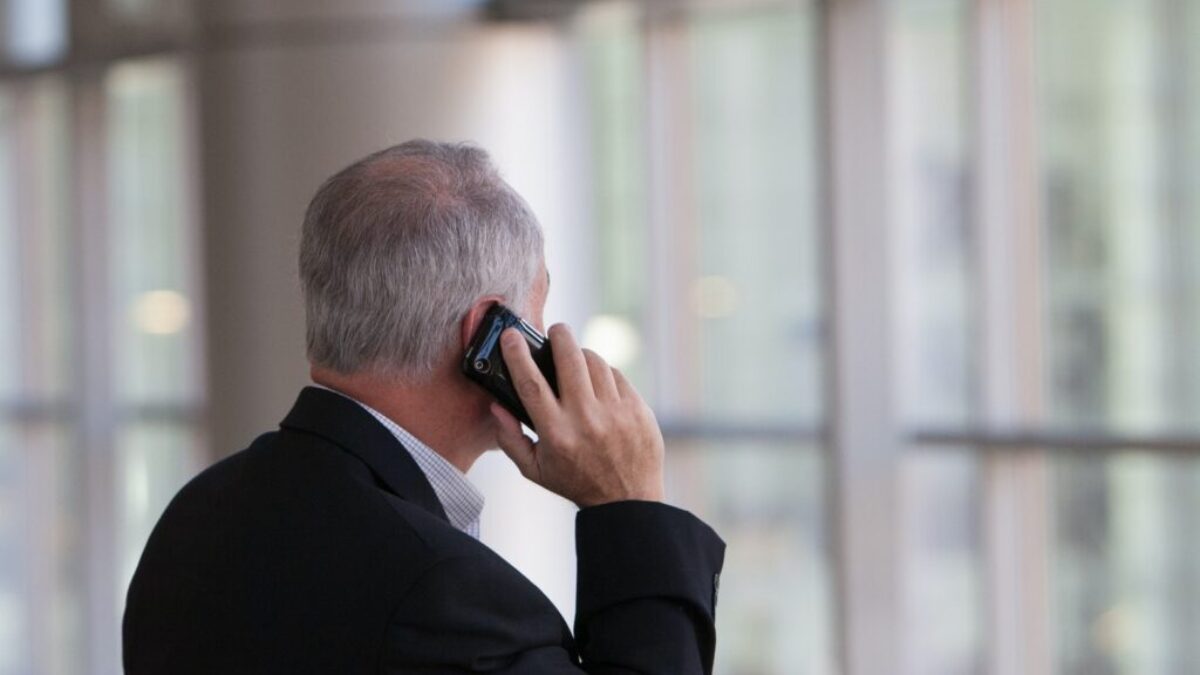 man holding black smartphone in front of a windowpane