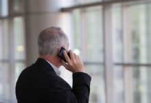 man holding black smartphone in front of a windowpane
