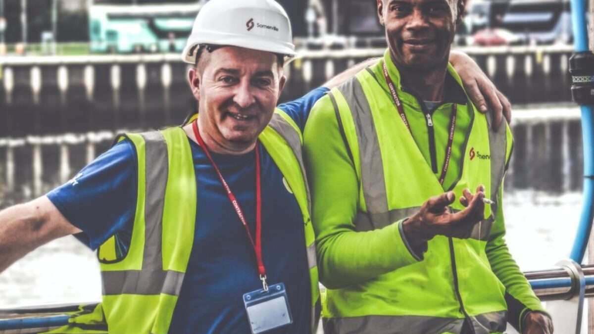selective focus photography of two men standing side by side wearing green reflective vests