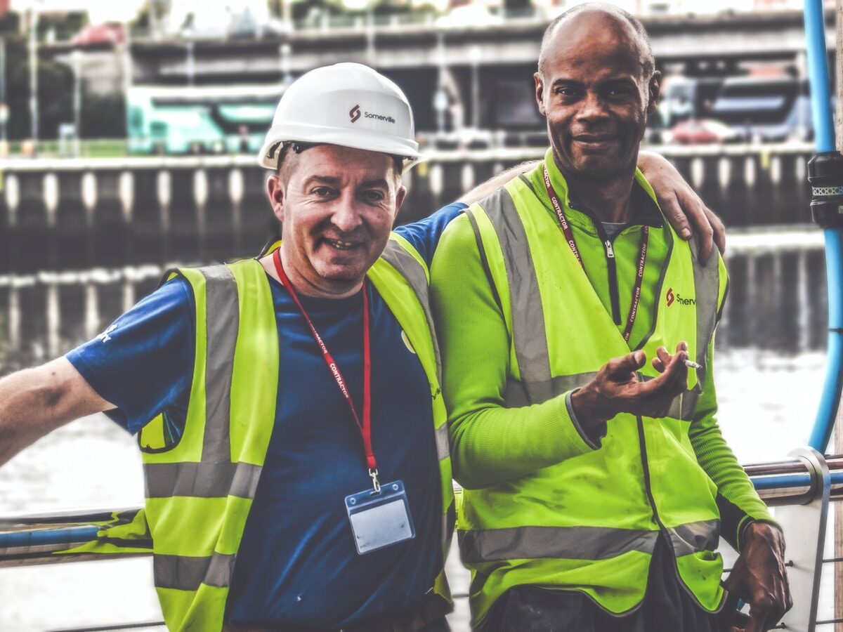 selective focus photography of two men standing side by side wearing green reflective vests
