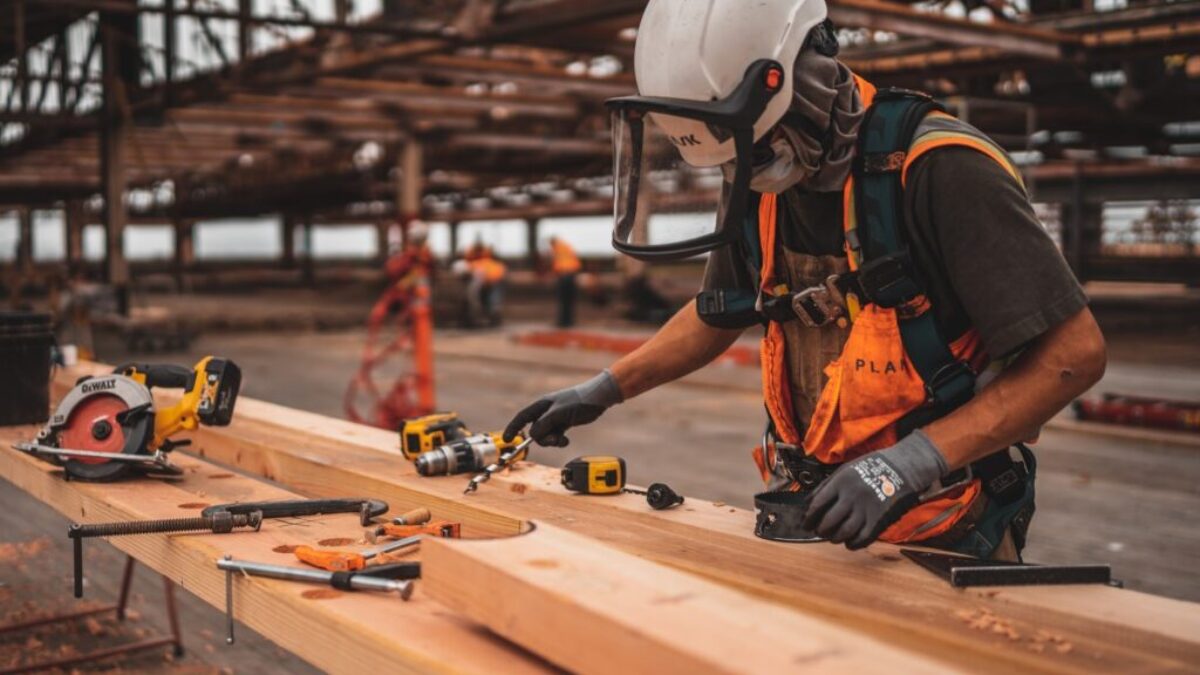man in orange and black vest wearing white helmet holding yellow and black power tool