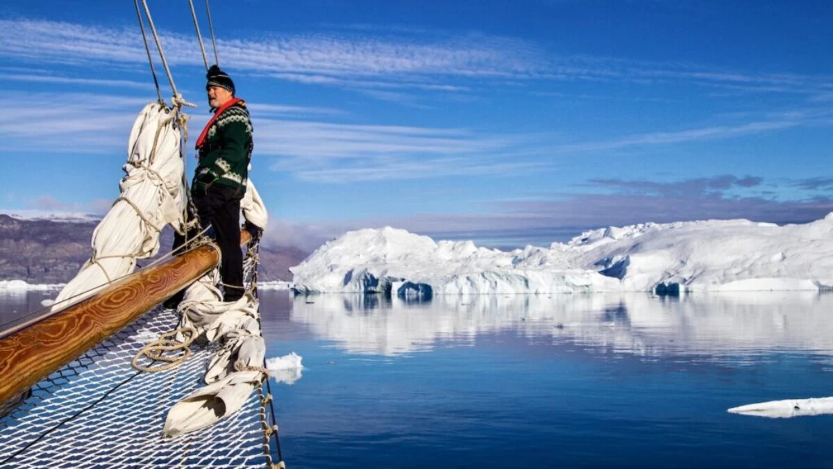 man in green jacket and blue denim jeans standing on brown wooden dock over snow covered