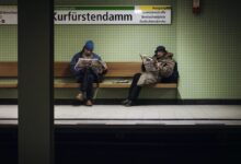 two men sitting on brown wooden bench reading magazines