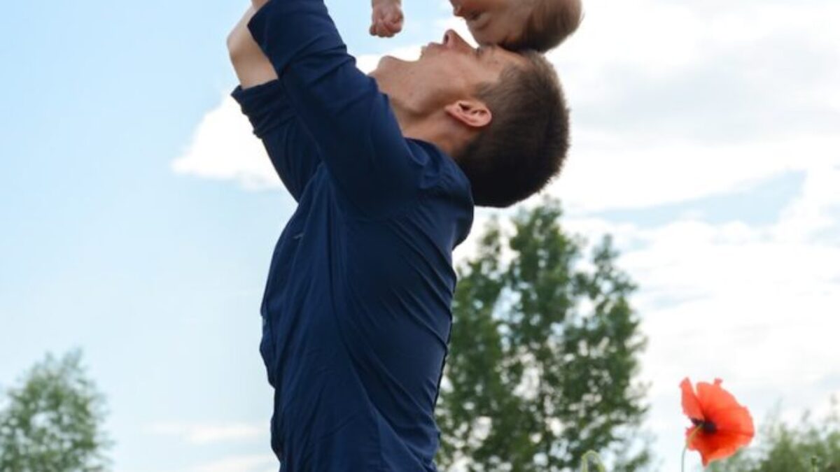 man in blue long sleeve shirt carrying baby in white onesie