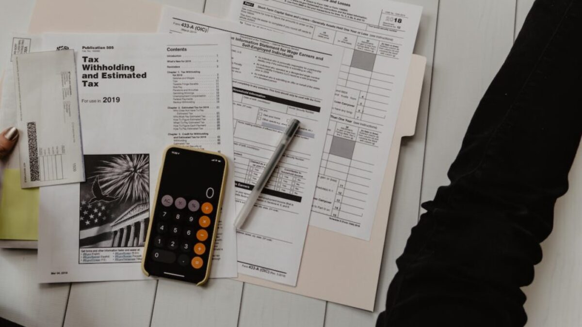 person holding paper near pen and calculator