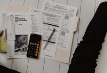 person holding paper near pen and calculator