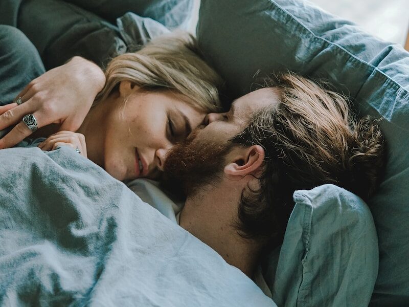 man kissing woman's forehead while lying on bed