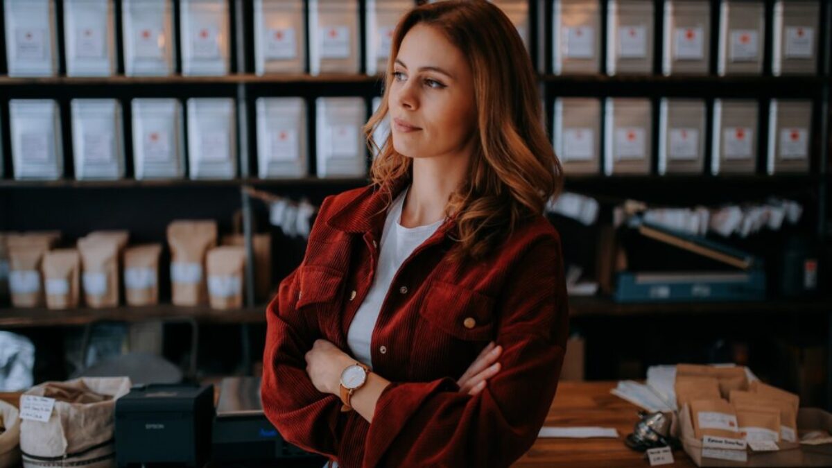 woman in brown jacket standing near black computer monitor