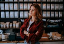 woman in brown jacket standing near black computer monitor