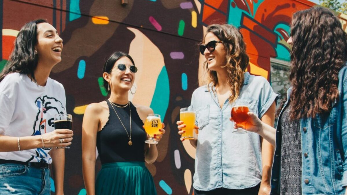 four women holding drinks while laughing together during daytime