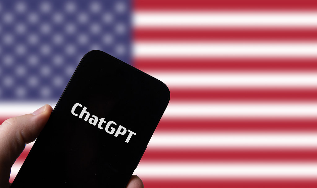 Hand holding smartphone with OpenAI Chat GPT against flag of USA - ByznysDeník