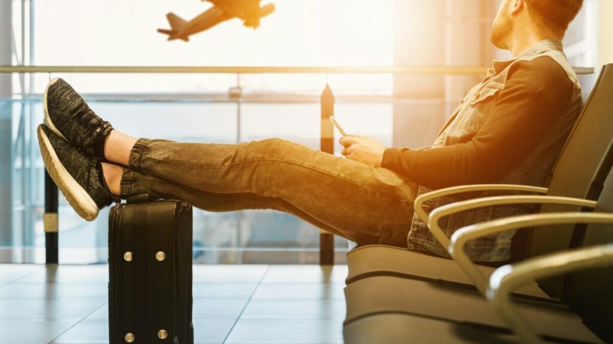 man sitting on gang chair with feet on luggage looking at airplane