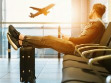 man sitting on gang chair with feet on luggage looking at airplane