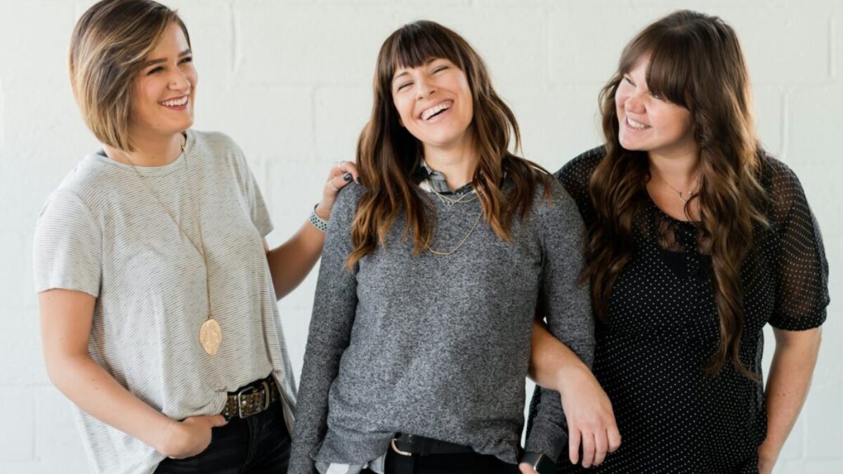 3 women smiling and standing beside white wall