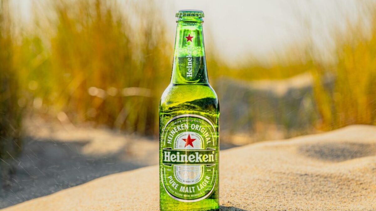 a bottle of beer sitting on top of a sandy beach