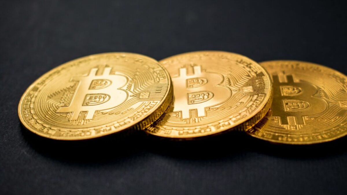 three gold-colored bitcoins on black surface