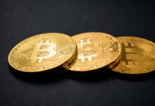 three gold-colored bitcoins on black surface