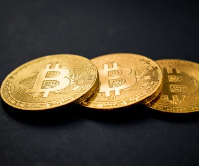 three gold-colored bitcoins on black surface