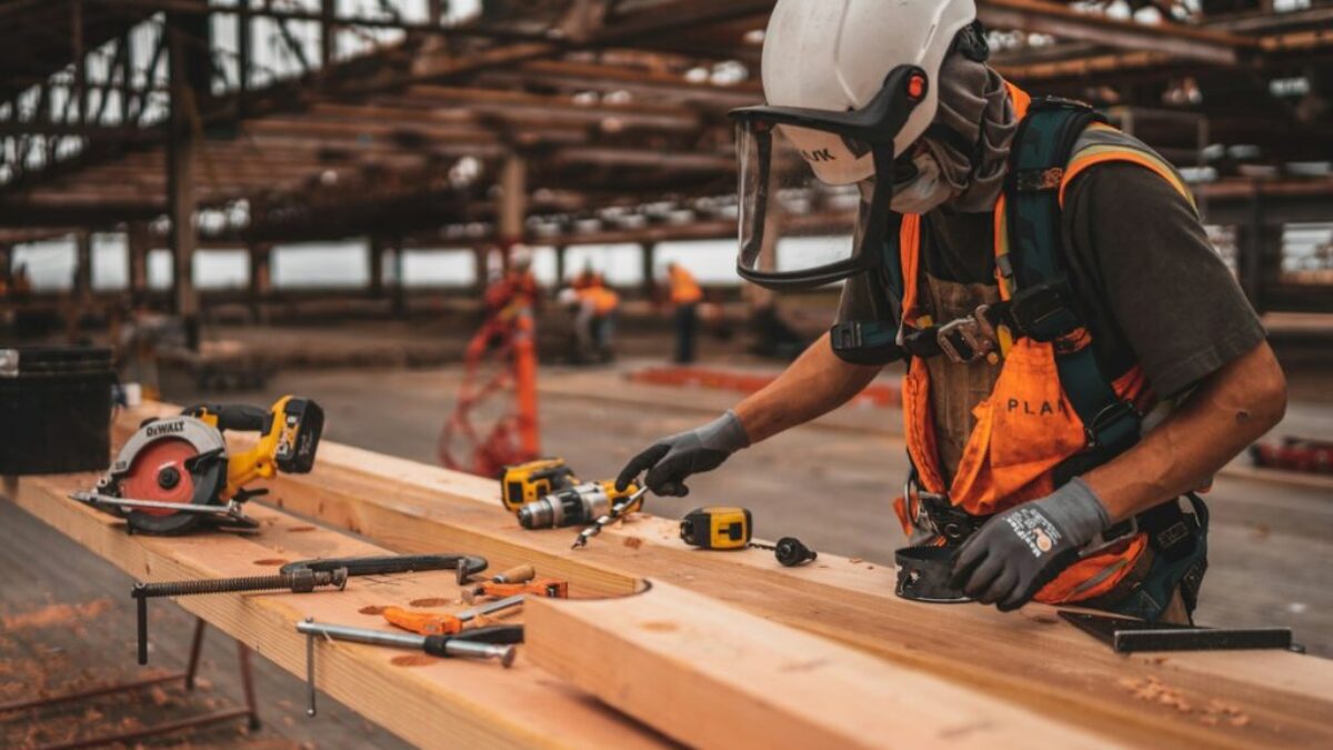 man in orange and black vest wearing white helmet holding yellow and black power tool