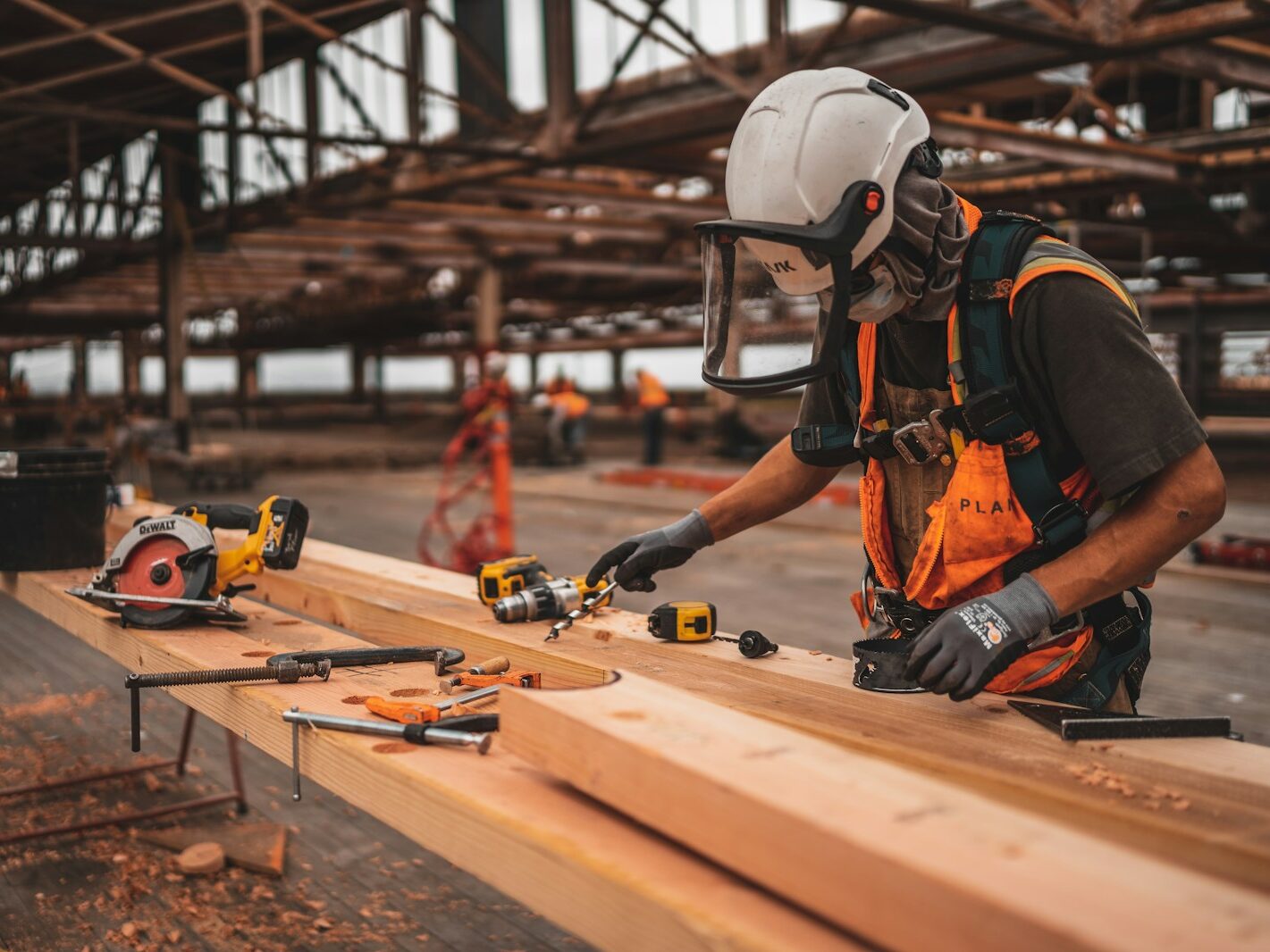 man in orange and black vest wearing white helmet holding yellow and black power tool