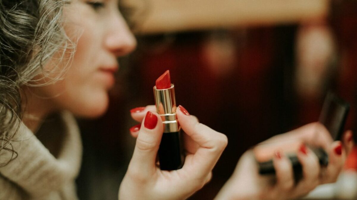 woman in gray sweater holding lipstick
