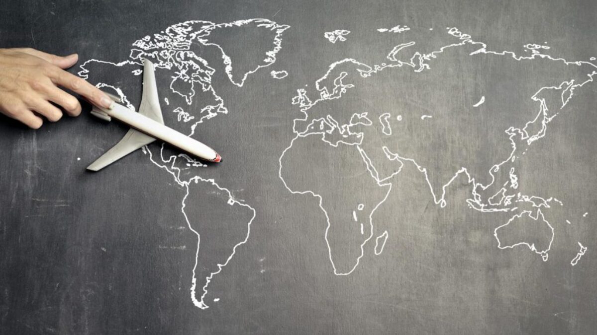 From above of crop anonymous person driving toy airplane on empty world map drawn on blackboard representing travel concept