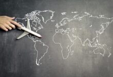 From above of crop anonymous person driving toy airplane on empty world map drawn on blackboard representing travel concept
