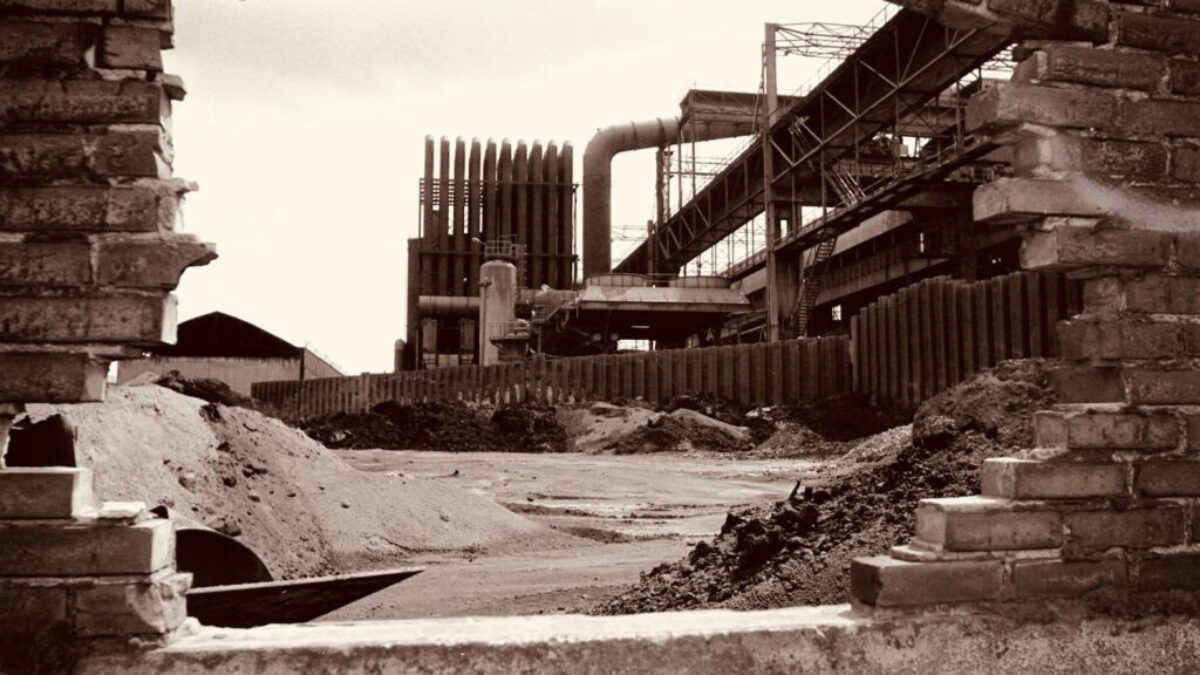 Sepia-toned view of an abandoned factory in Charleroi, Belgium, through a brick wall.