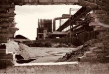 Sepia-toned view of an abandoned factory in Charleroi, Belgium, through a brick wall.