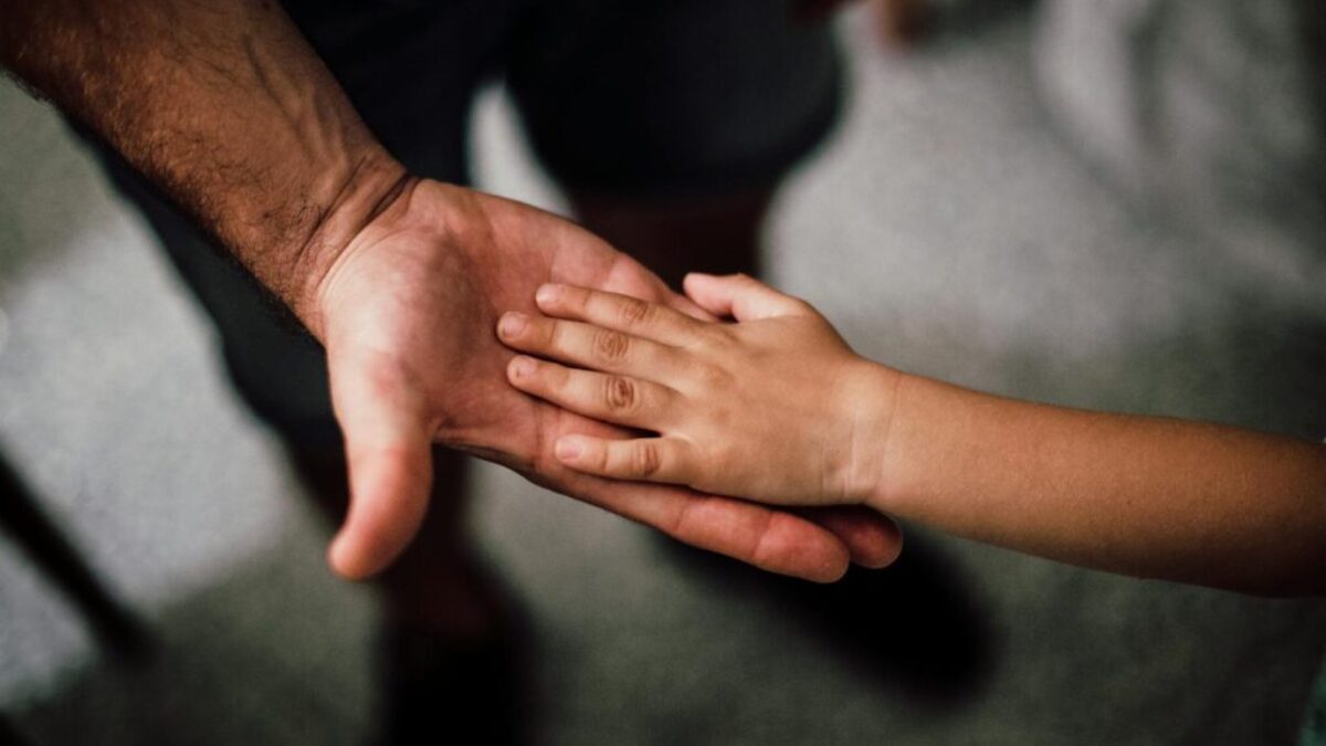 Close-up of a child's hand resting gently on a man's hand, symbolizing love and support.
