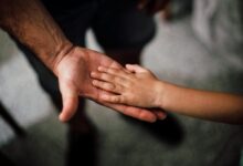 Close-up of a child's hand resting gently on a man's hand, symbolizing love and support.