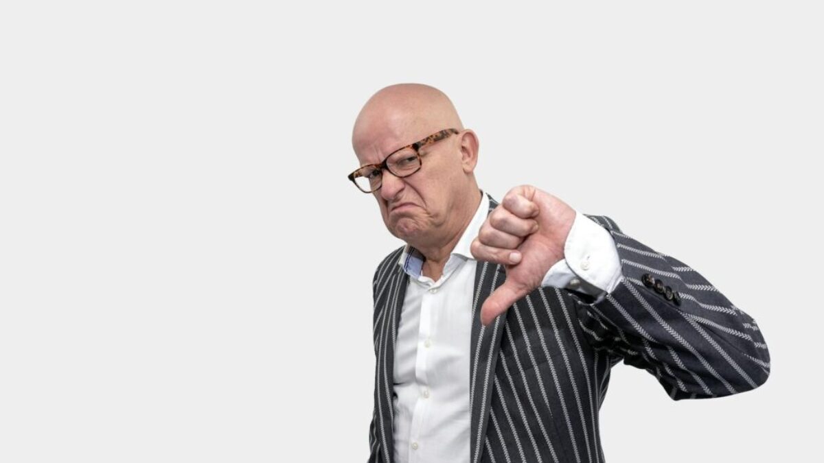 Bald businessman in striped coat giving a thumbs down gesture against a white background.