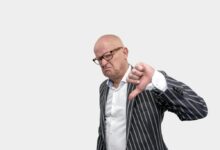 Bald businessman in striped coat giving a thumbs down gesture against a white background.