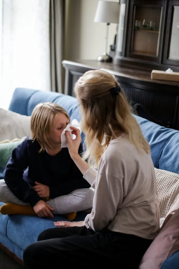 Photo by cottonbro studio - ByznysDeník A mother tends to her sick child with a tissue on the couch, showcasing care and comfort.