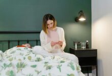 A mother beside her sick child holding medicine in a cozy bedroom setting.