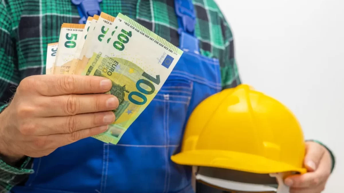 Muž u montérkách a s helmou drží eura