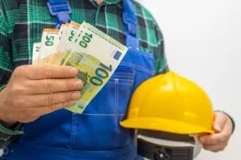 Muž u montérkách a s helmou drží eura