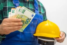 Muž u montérkách a s helmou drží eura