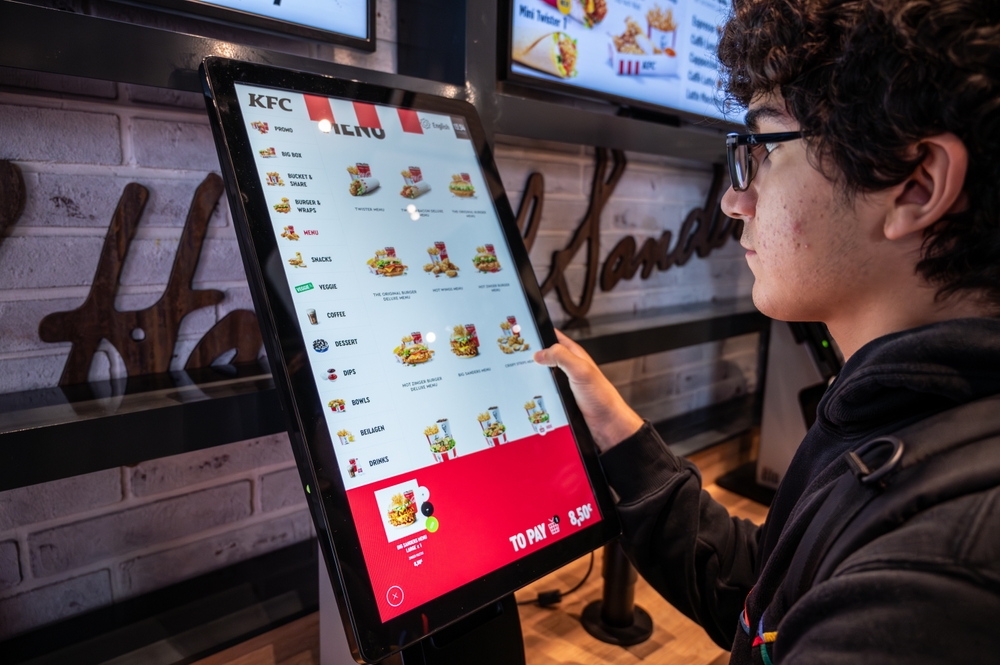 Mladý muž si objednává na obrazovce jídlo v KFC