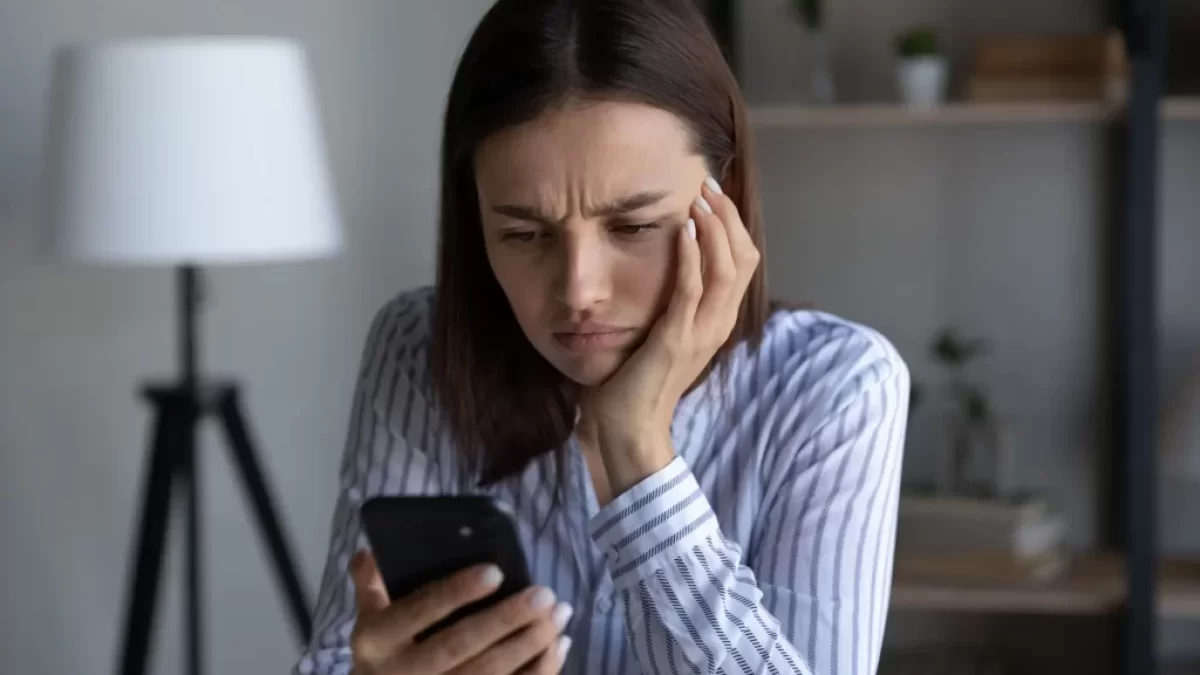 Frustrovaná žena sledující svůj telefon