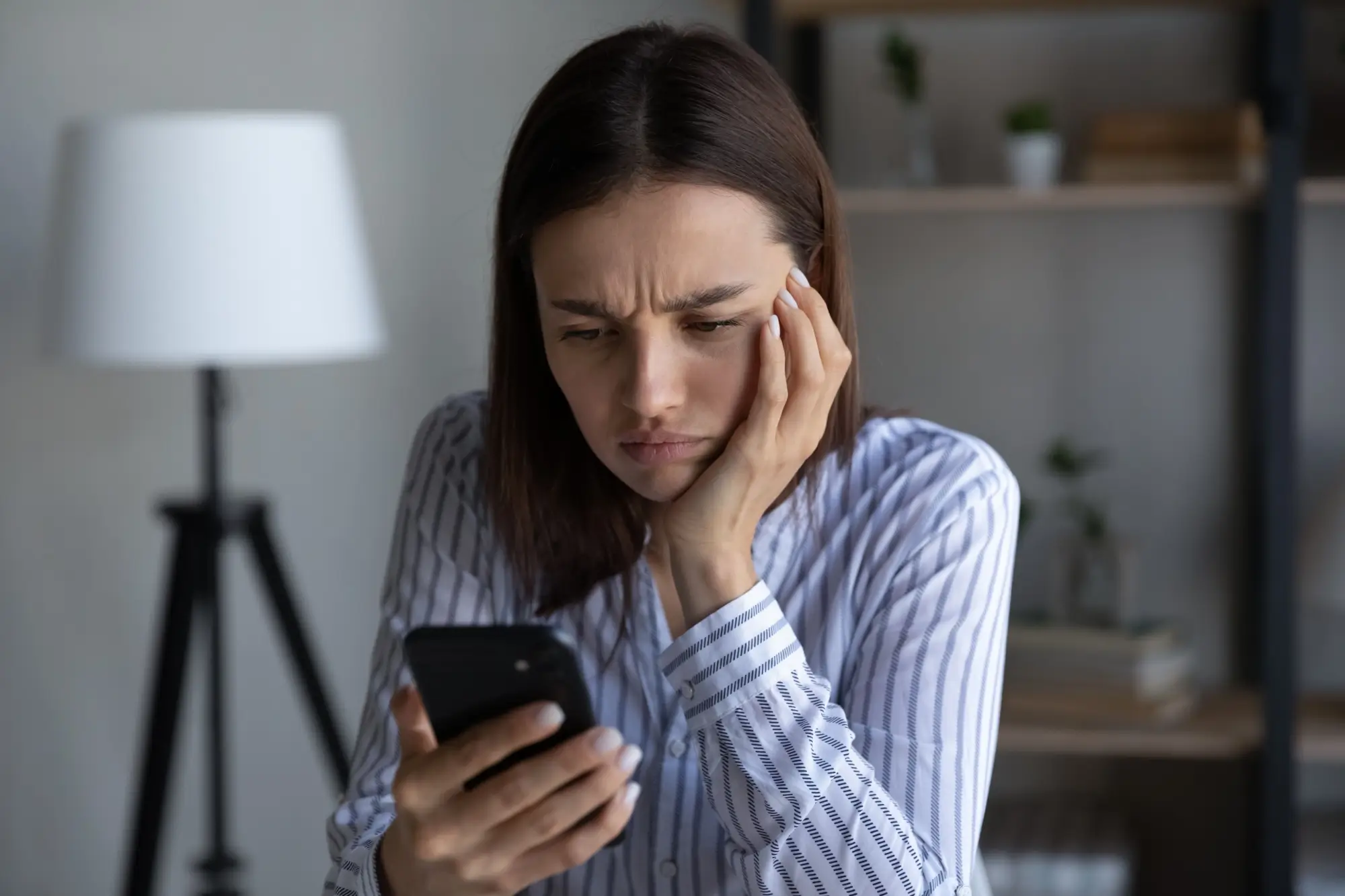 Frustrovaná žena sledující svůj telefon